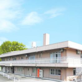 介護施設の建物外観。平屋から2階建ての白とベージュ色の施設建物